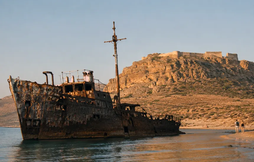 Rusted Dimitrios shipwreck on Gramvousa Island beach with the Venetian fortress above at sunset.