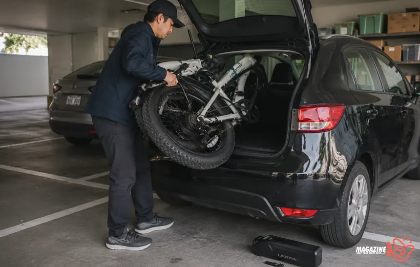 Person loading a folded fat tire e-bike into a hatchback inside a parking garage