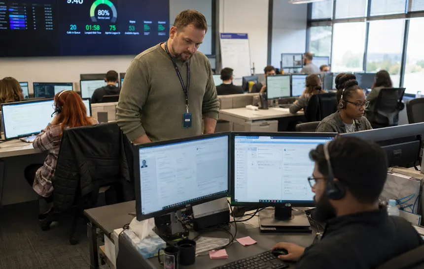 Customer support agents managing incoming calls in a modern office with live dashboards and headset communication.