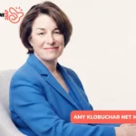 Amy Klobuchar smiling in blue blazer, seated in gray armchair for portrait
