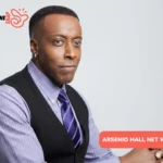 Arsenio Hall net worth photo: seated portrait in vest and purple striped tie