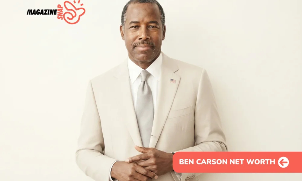 Ben Carson Net Worth: man in tan suit with flag pin, hands clasped, cream backdrop