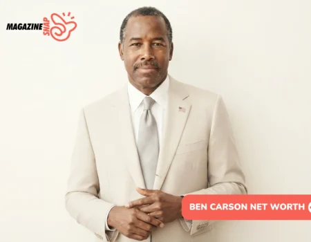 Ben Carson Net Worth: man in tan suit with flag pin, hands clasped, cream backdrop