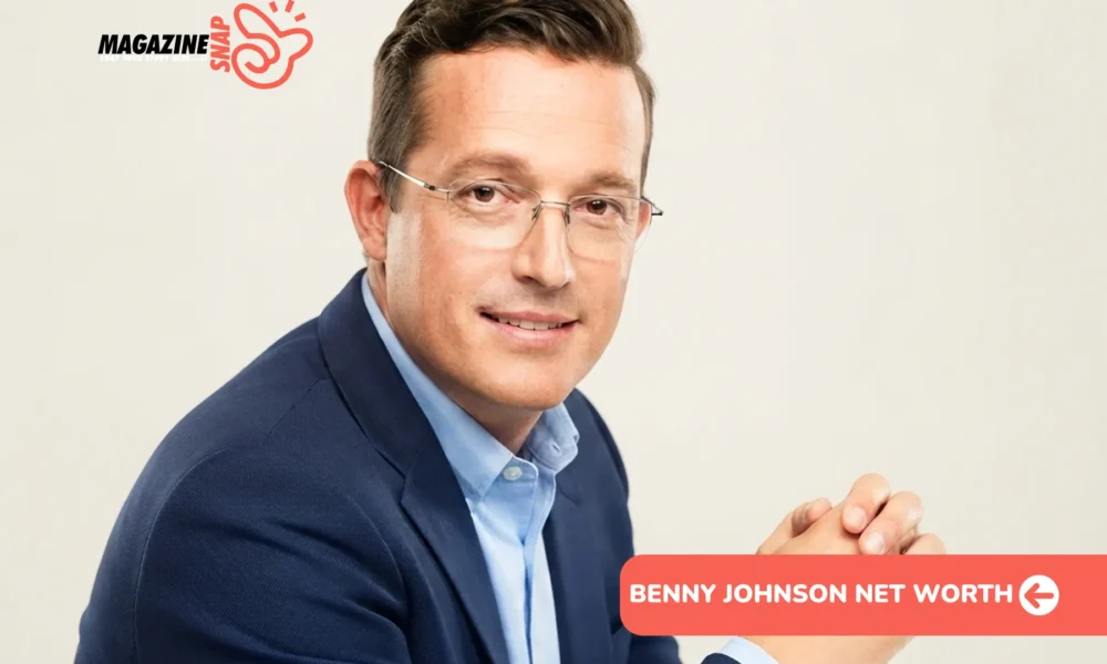 Benny Johnson net worth profile photo: seated headshot in navy blazer