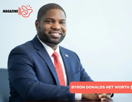 Byron Donalds smiling in navy suit and red tie, seated at wooden desk
