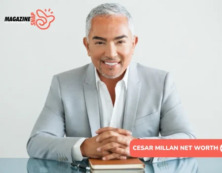 Cesar Millan Net Worth - gray-haired man in gray suit smiling at glass desk with notebook