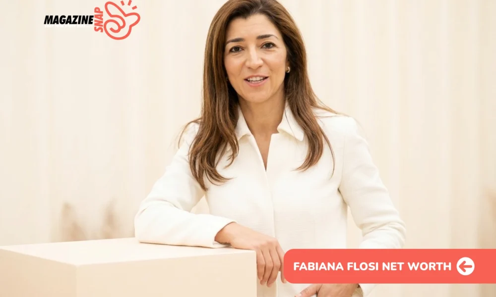 Fabiana Flosi smiling in a white blazer, leaning on a cream pedestal in a studio portrait