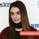 Aimee Osbourne in a burgundy jacket at a media event, pictured for the Aimee Osbourne net worth article.