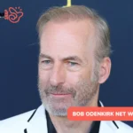 Bob Odenkirk in white blazer and black shirt against navy backdrop, bob odenkirk net worth article