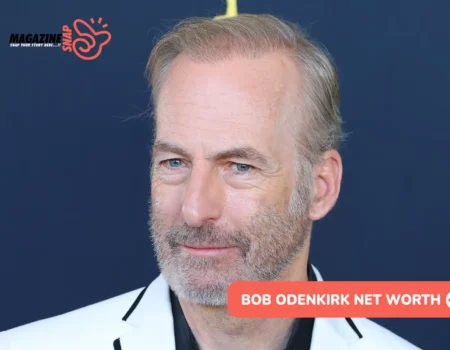 Bob Odenkirk in white blazer and black shirt against navy backdrop, bob odenkirk net worth article