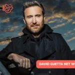 David Guetta net worth leans on a rooftop railing at dusk in a dark coat for the article.