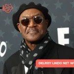 Delroy Lindo net worth article portrait: black beret, tinted glasses, and scarf at a red carpet event.
