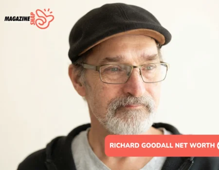 Richard Goodall net worth portrait: close-up in flat cap, glasses, and gray beard against plain background