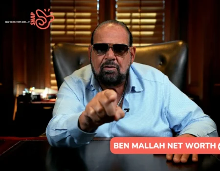 Ben Mallah net worth portrait, pointing at camera from a wood-paneled office desk.