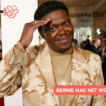 Bernie Mac net worth article portrait, smiling on a red carpet in a patterned blazer