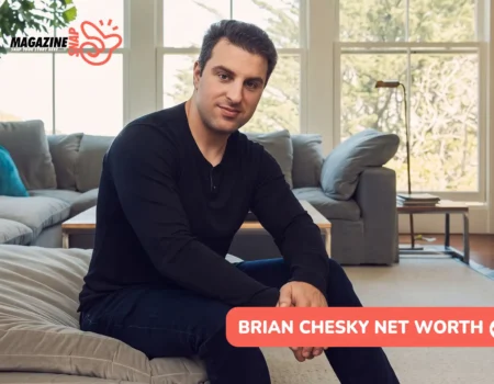 Airbnb CEO Brian Chesky sitting on a grey sofa in a bright living room, wearing a black long-sleeve shirt