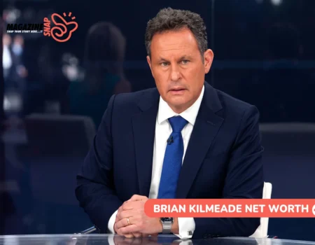 Brian Kilmeade seated at news desk in navy suit for net worth article