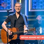 Bryan Adams net worth article photo: smiling guitarist in a black shirt at a microphone, drummer behind