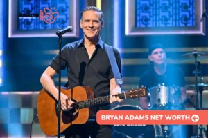 Bryan Adams net worth article photo: smiling guitarist in a black shirt at a microphone, drummer behind