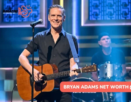 Bryan Adams net worth article photo: smiling guitarist in a black shirt at a microphone, drummer behind