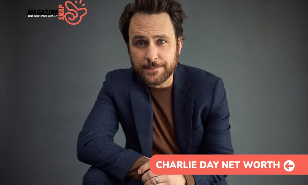 Charlie Day net worth article portrait of a bearded man in a navy blazer against a plain gray backdrop