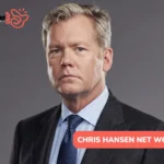 Chris Hansen net worth article portrait: man in a charcoal suit and navy tie on a gray studio backdrop