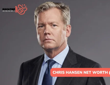 Chris Hansen net worth article portrait: man in a charcoal suit and navy tie on a gray studio backdrop