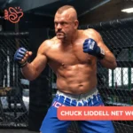 Chuck Liddell net worth article photo: fighter in blue gloves and shorts in a fighting stance beside a cage