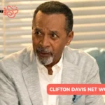Clifton Davis in a light gray blazer and white shirt on a teal sofa, for the Clifton Davis net worth article