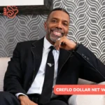 Creflo Dollar net worth article portrait of him smiling in a black suit and tie, seated in a striped armchair