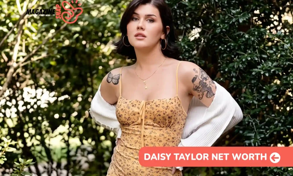 Daisy Taylor net worth article image: yellow floral dress, white cardigan, hands on hips among shrubs