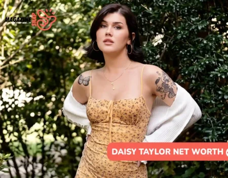 Daisy Taylor net worth article image: yellow floral dress, white cardigan, hands on hips among shrubs